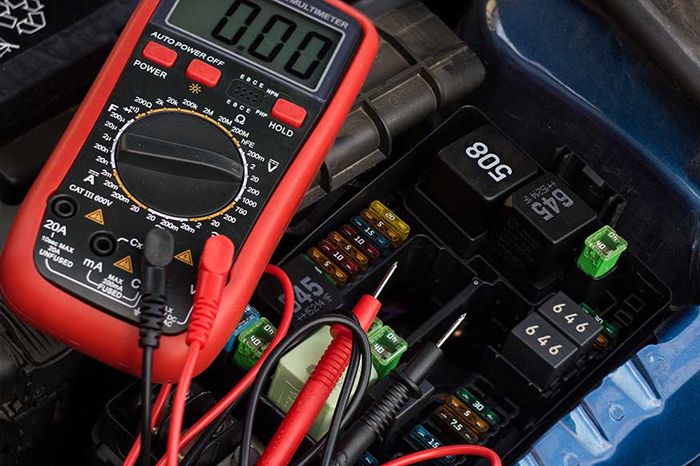 Mechanic wearing protective gloves removing a car battery from the engine bay